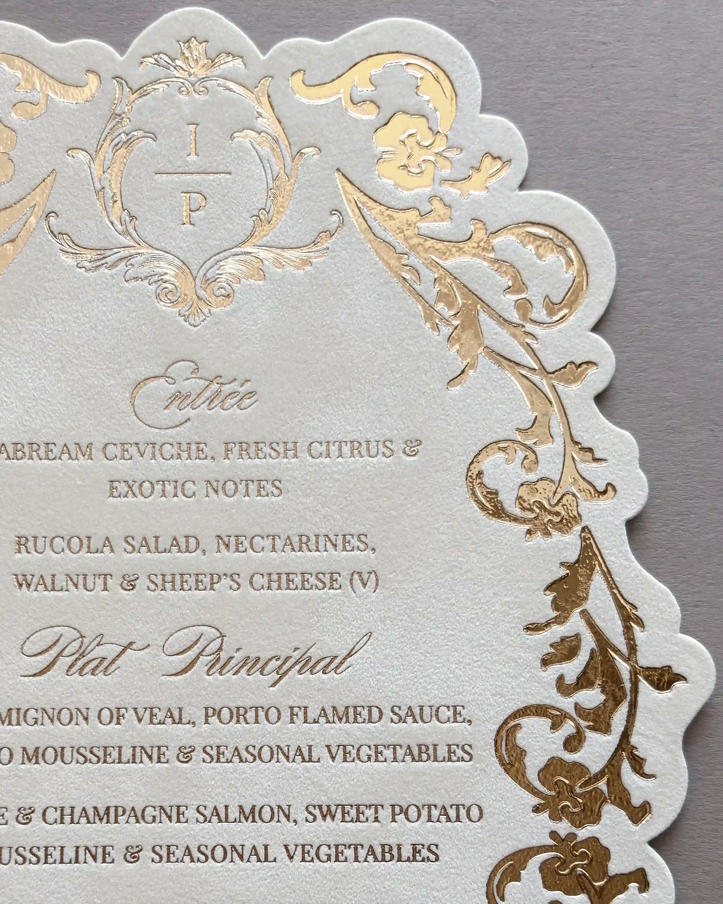 Close-up of Belle wedding menu monogram crest and gold foil-pressed floral filigree with printed entrée and main course details | Polina Perri