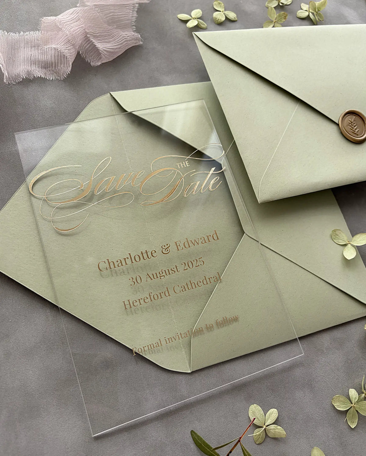 Clear Acrylic Save the Date card with gold foil calligraphy and wedding details laid on open sage green envelope, sealed envelope with gold wax seal behind — Polina Perri