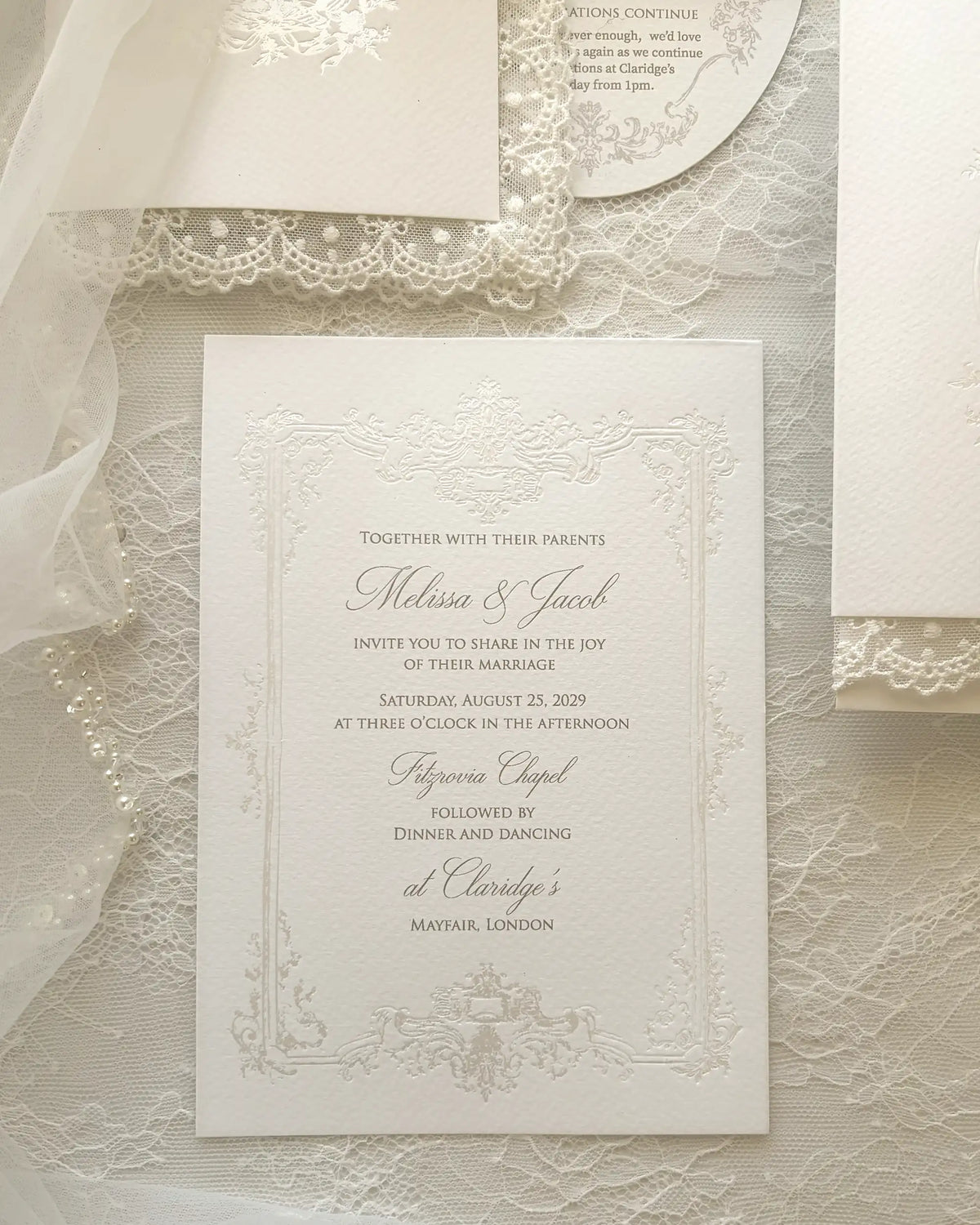 Alyson Lace White square wedding invitation card with ornate embossed floral borders, digitally printed wording on lace and ribbon background, white envelope with round tag included — Polina Perri. 