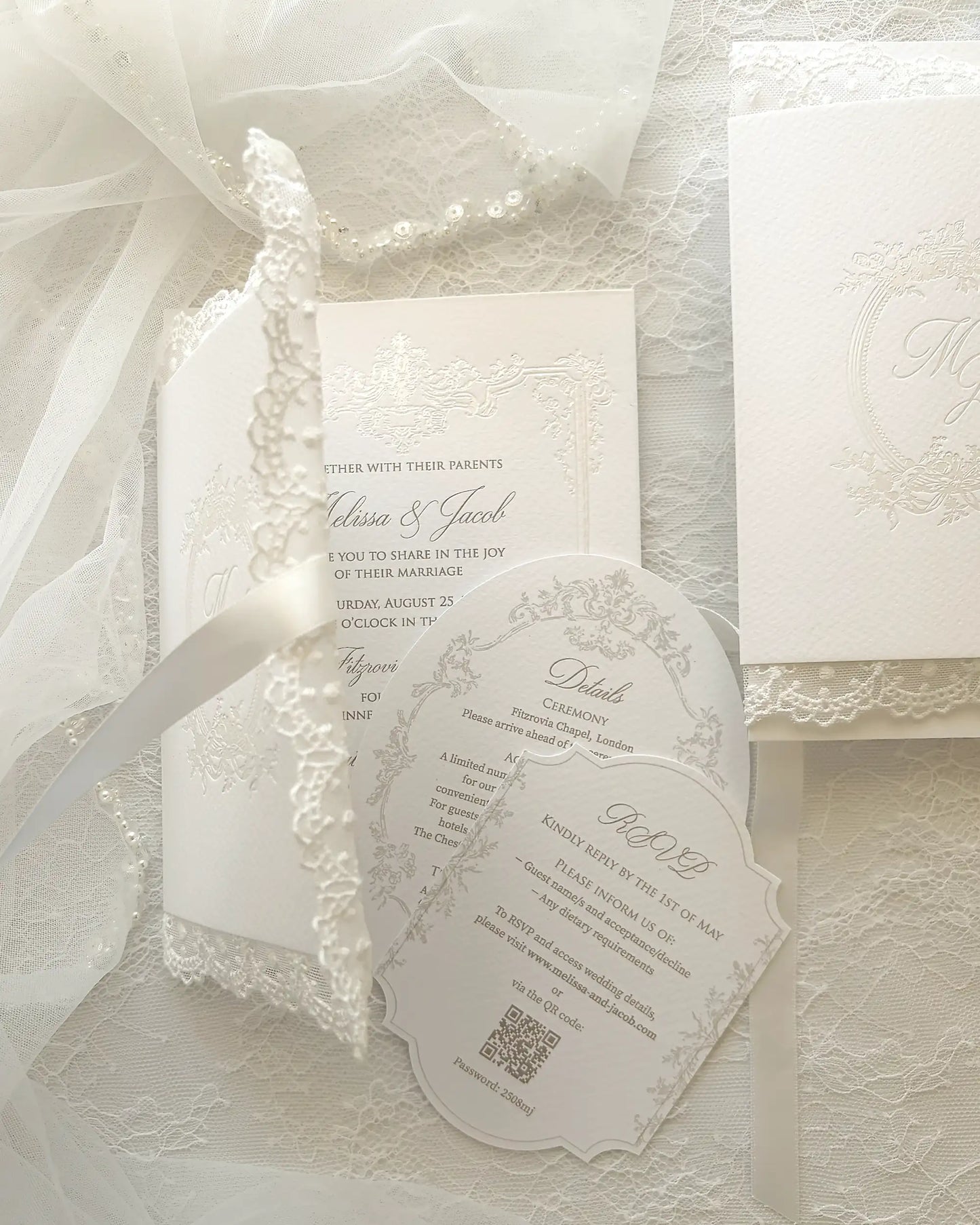 Alyson Lace White complete wedding invitation suite with embossed floral details, invitation card, RSVP card with shaped edges, white envelope and silk ribbon on delicate lace fabric background — Polina Perri. 