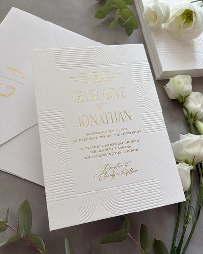 Art Deco wedding invitation with embossed wave-pattern and gold foil details arranged in flat lay with white roses and green eucalyptus leaves, matching envelope partially visible — Polina Perri