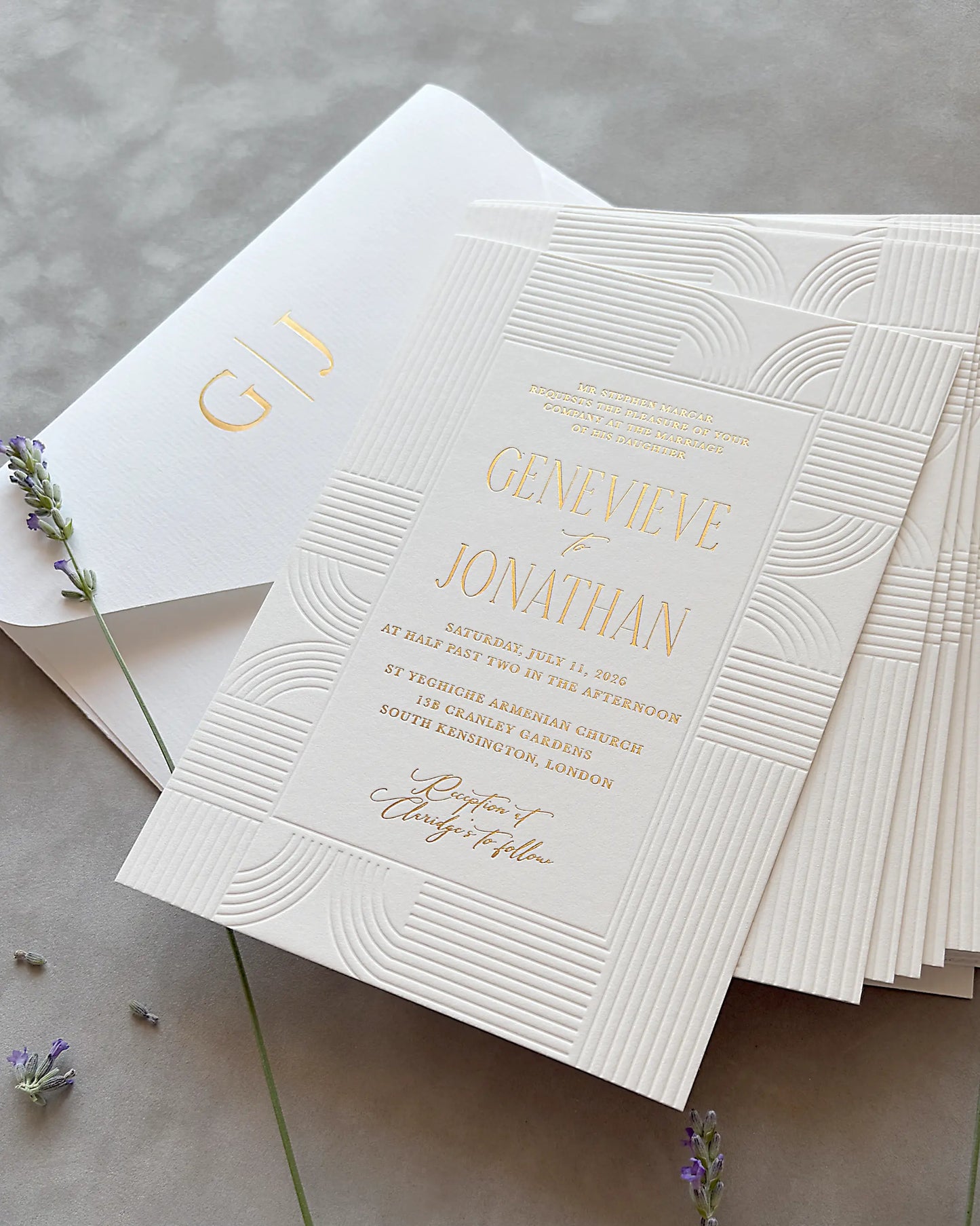 Stack of Art Deco wedding invitations with embossed wave patterns and gold foil lettering, matching envelope and dried lavender sprigs on neutral gray surface — Polina Perri