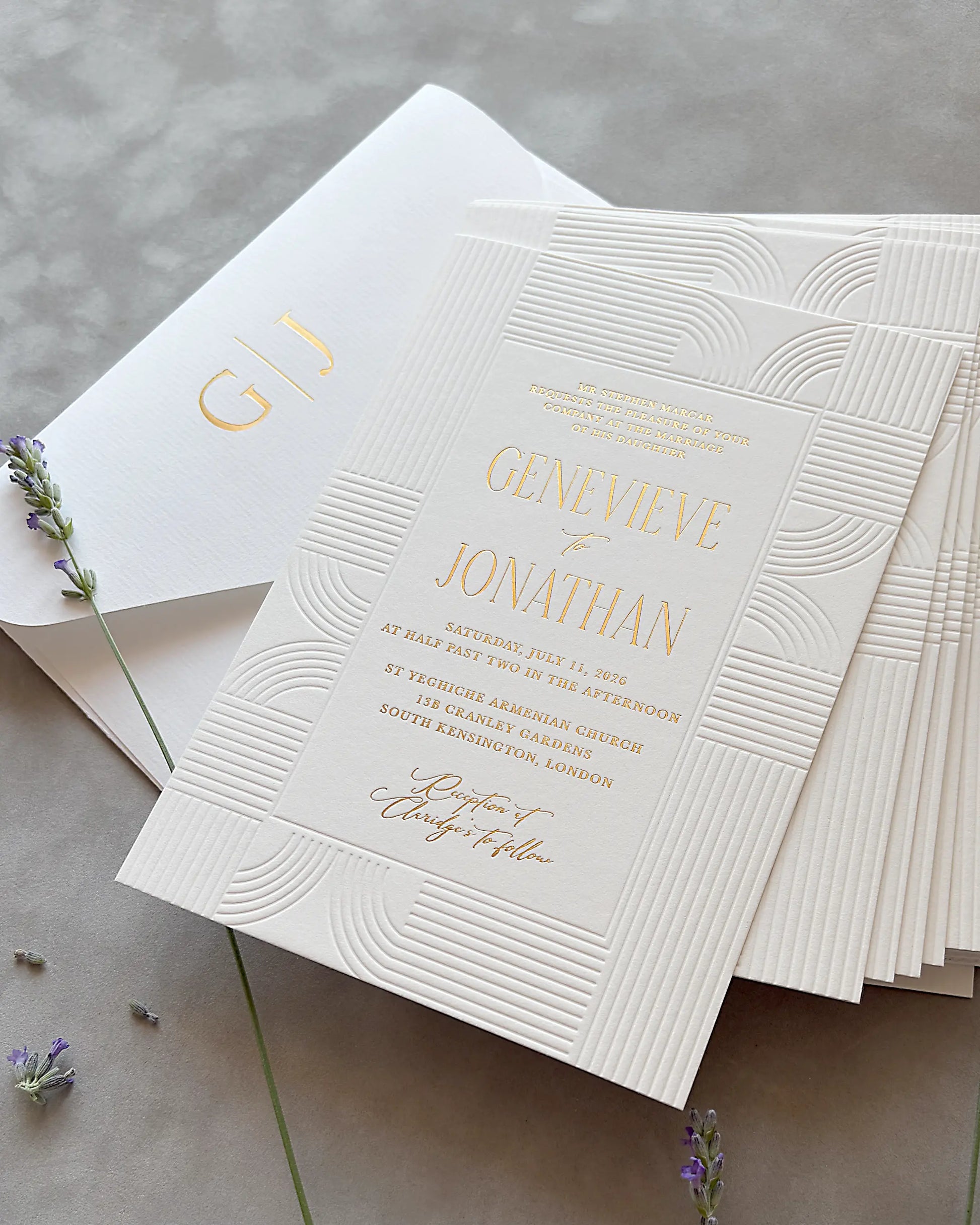 Stack of Art Deco wedding invitations with embossed wave patterns and gold foil lettering, matching envelope and dried lavender sprigs on neutral gray surface — Polina Perri