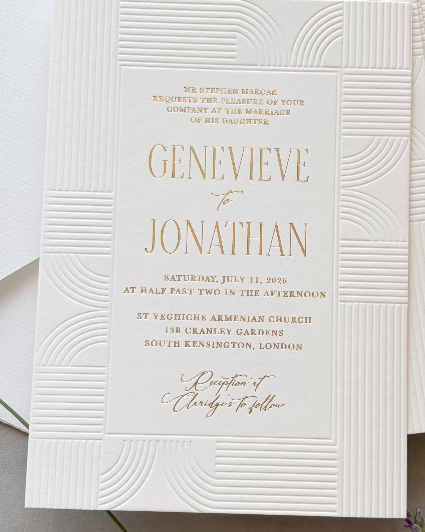Art Deco invitation displaying embossed geometric wave-pattern frame and gold foil couple's names with complete wedding details, coordinated white envelope layered and visible behind — Polina Perri
