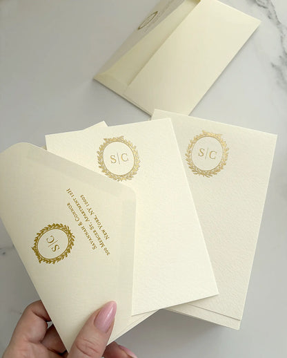 Hand holding cream thank you cards with a gold foil wreath monogram and an envelope flap foil-pressed with the return address