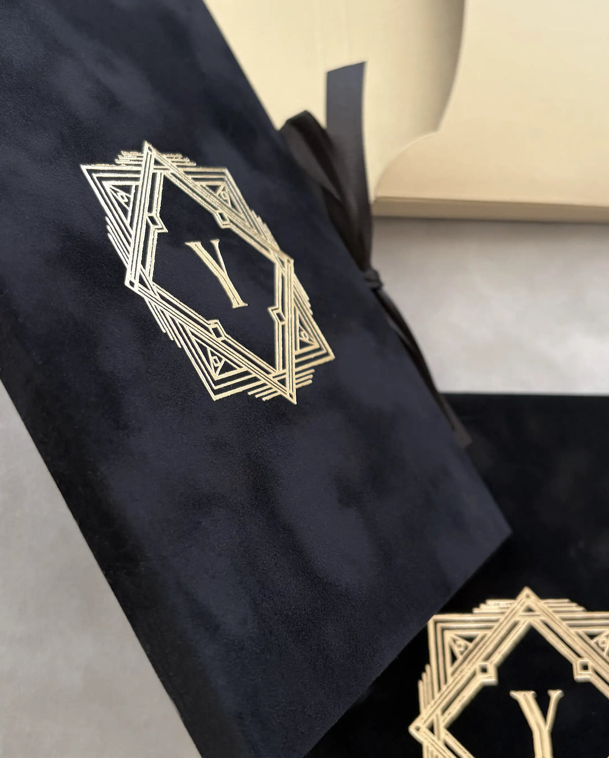 Great Gatsby Folio Invitation close-up of gold foil Art Deco monogram on black velvet cover with black ribbon tie — Polina Perri