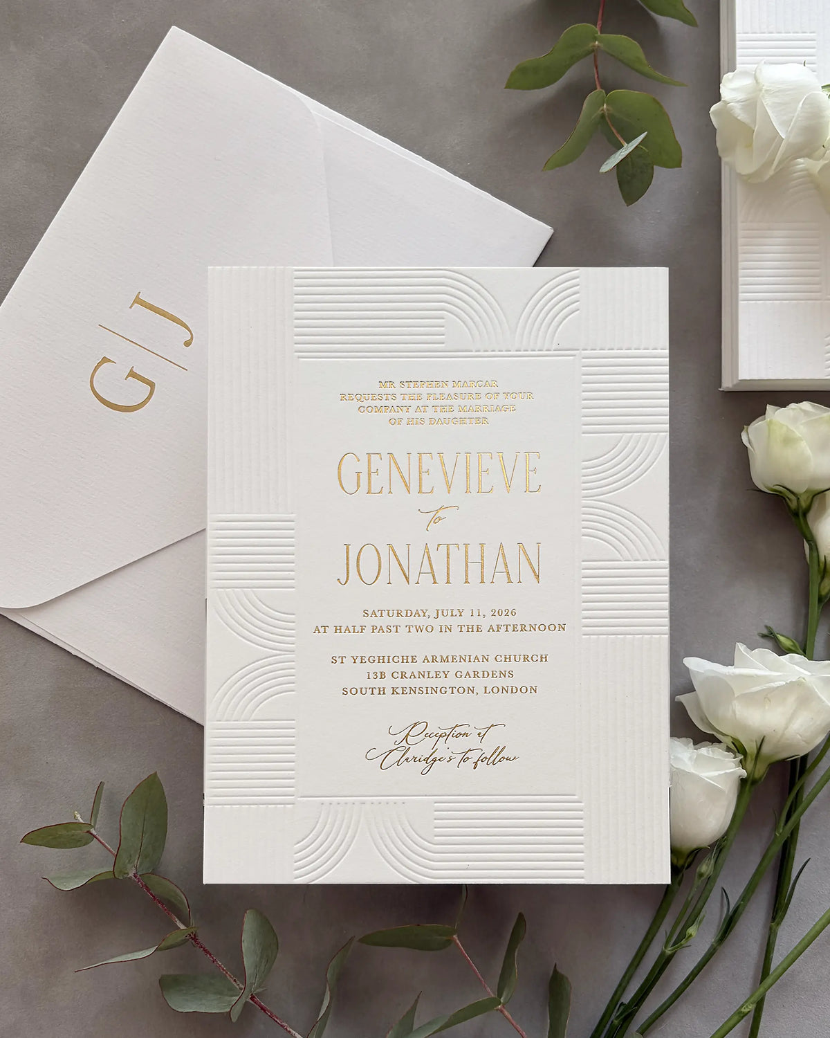 Modern Art Deco wedding invitation suite with gold foil couple's names and geometric wave-pattern design on white cotton paper, personalized envelope with gold foil monogram initials, styled with white roses and green leaves — Polina Perri. 