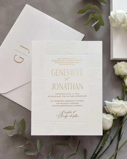 Modern Art Deco wedding invitation suite with gold foil couple's names and geometric wave-pattern design on white cotton paper, personalized envelope with gold foil monogram initials, styled with white roses and green leaves — Polina Perri. 