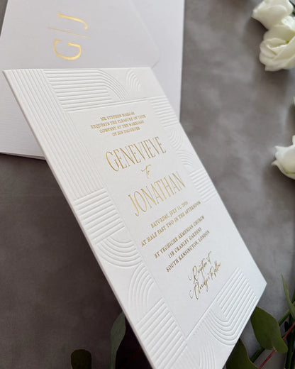 Modern Art Deco wedding stationery collection featuring monogrammed envelope and geometric wave invitation with gold foil details, arranged on neutral gray surface with florals — Polina Perri