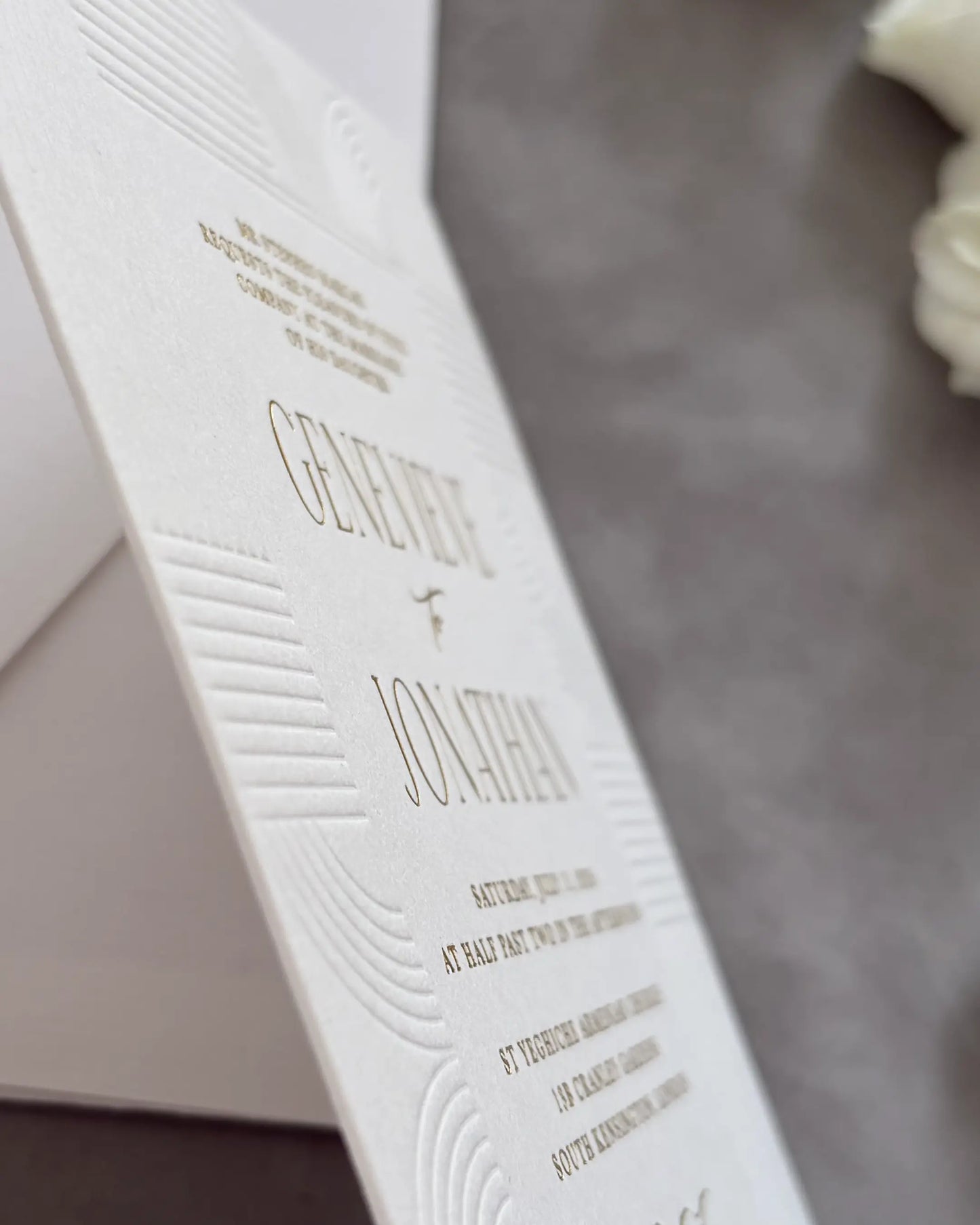 Modern Art Deco wedding invitation close-up with blind-embossed geometric lines and fine gold foil lettering on textured white cotton paper — Polina Perri